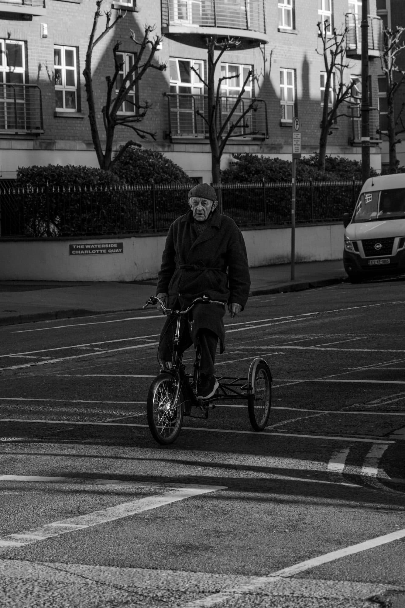 A man riding a tricycle across an empty junction at Charlotte Quay, Dublin