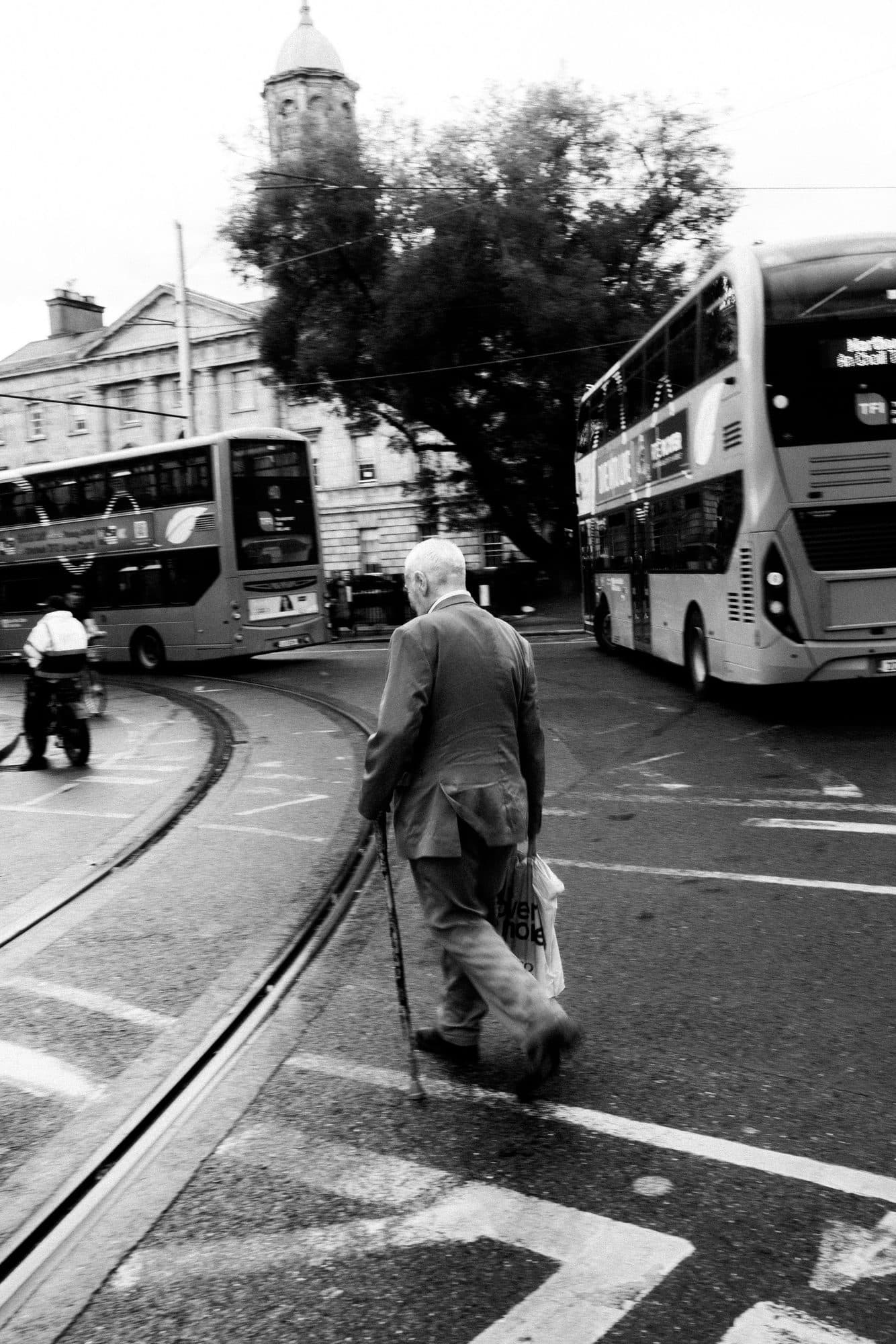 A man crossing tram tracks in Dublin, seen from behind, between two buses