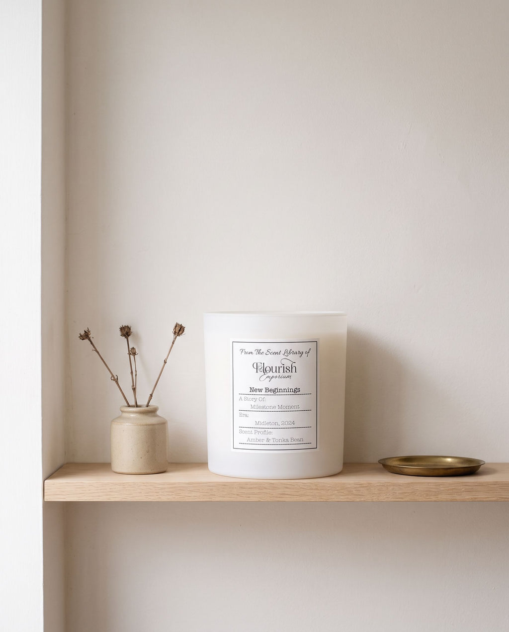 New Beginnings candle unlit on a pale oak shelf beside oatmeal stoneware and a brass tray