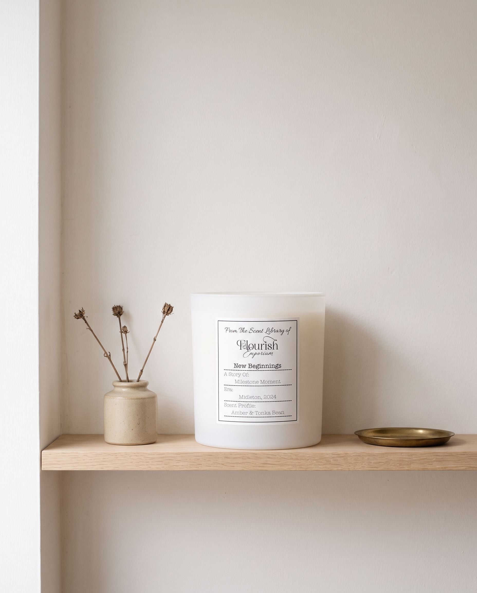 New Beginnings candle unlit on a pale oak shelf beside oatmeal stoneware and a brass tray