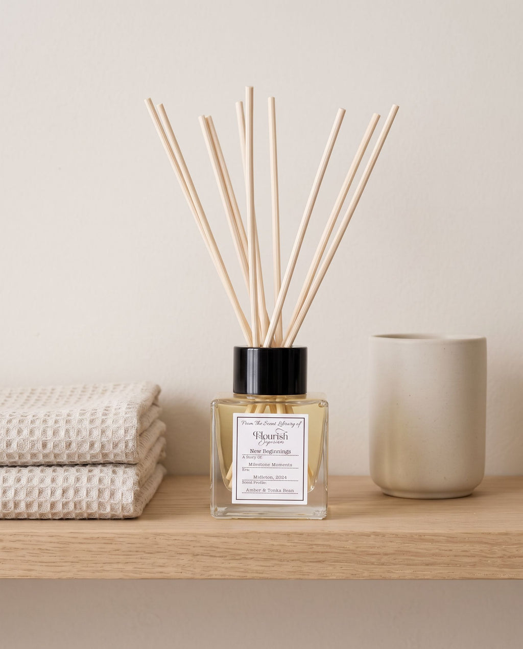 New Beginnings reed diffuser on a pale oak bathroom shelf beside folded linen towels