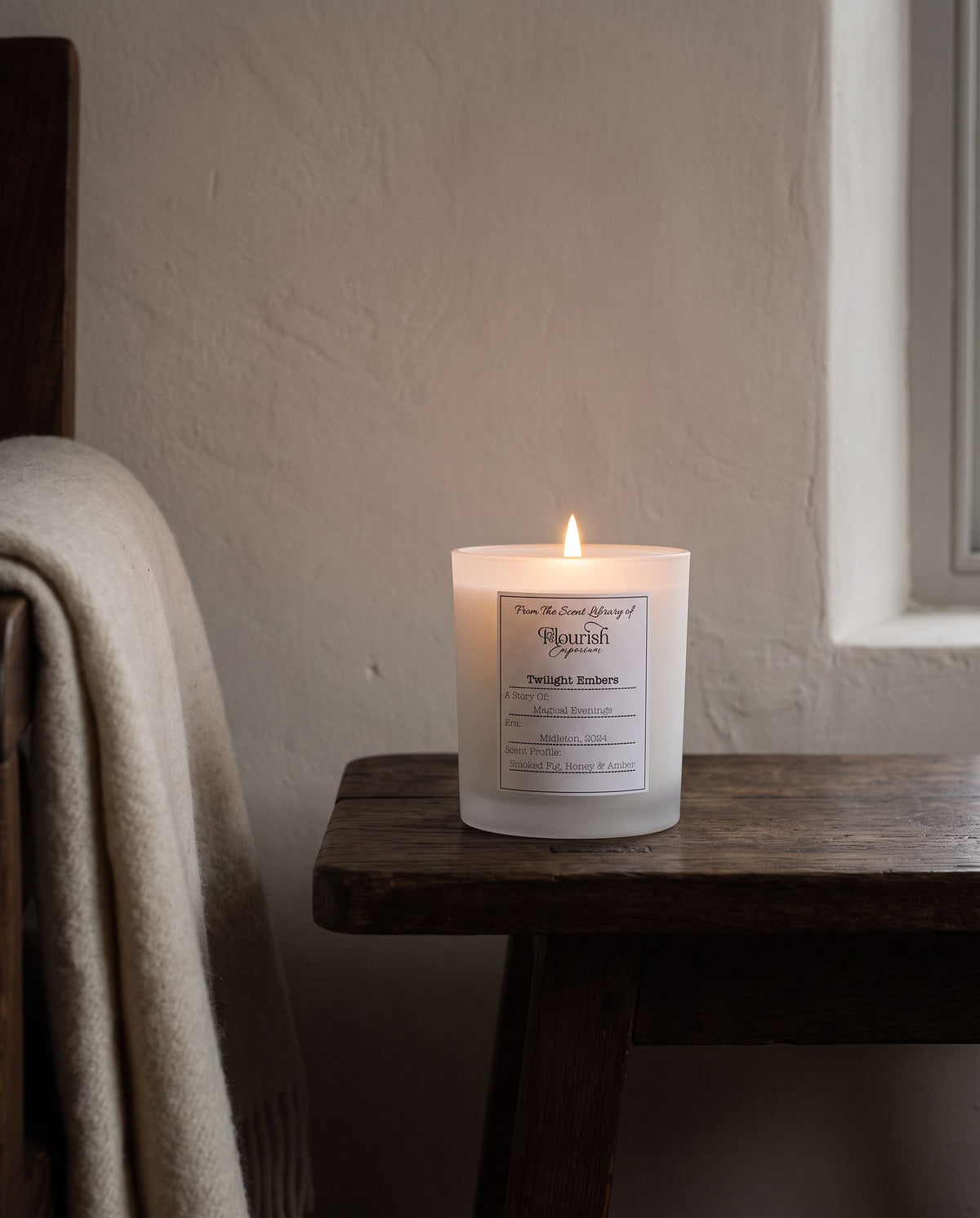 Twilight Embers candle lit on a dark timber table at dusk beside a cream wool throw